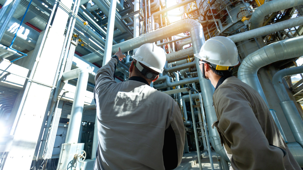 Two technicians examining an industrial boiler system in a plant environment.